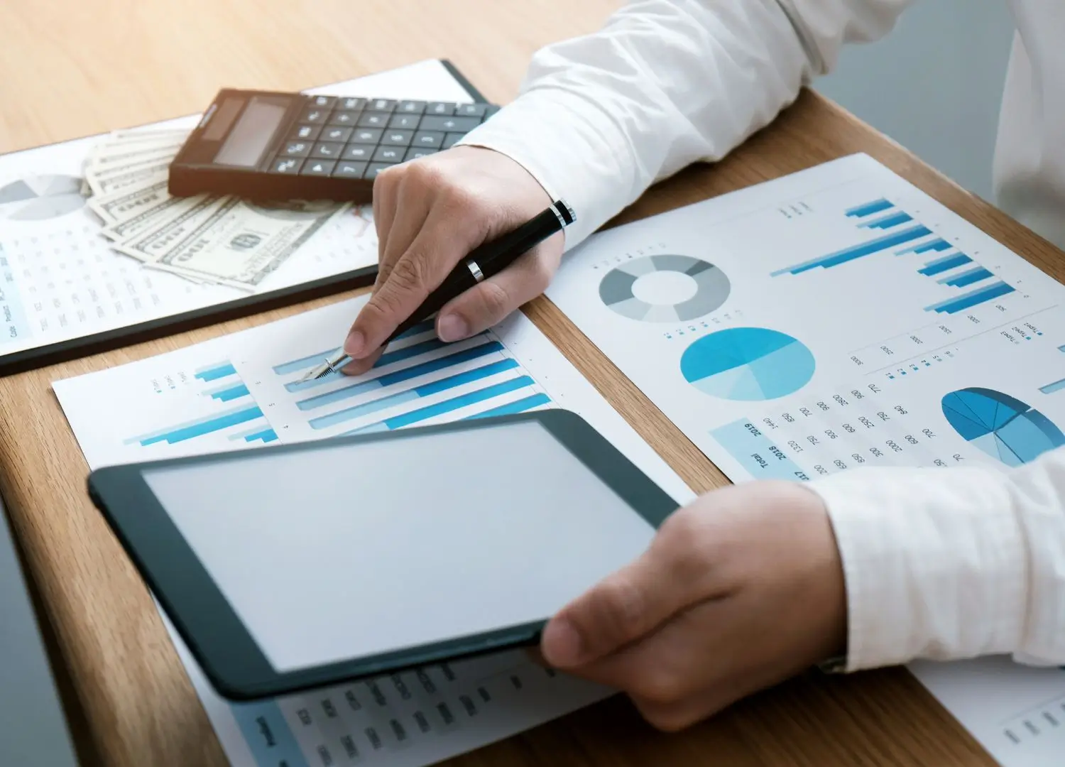 A person's hands working on a tablet with financial documents