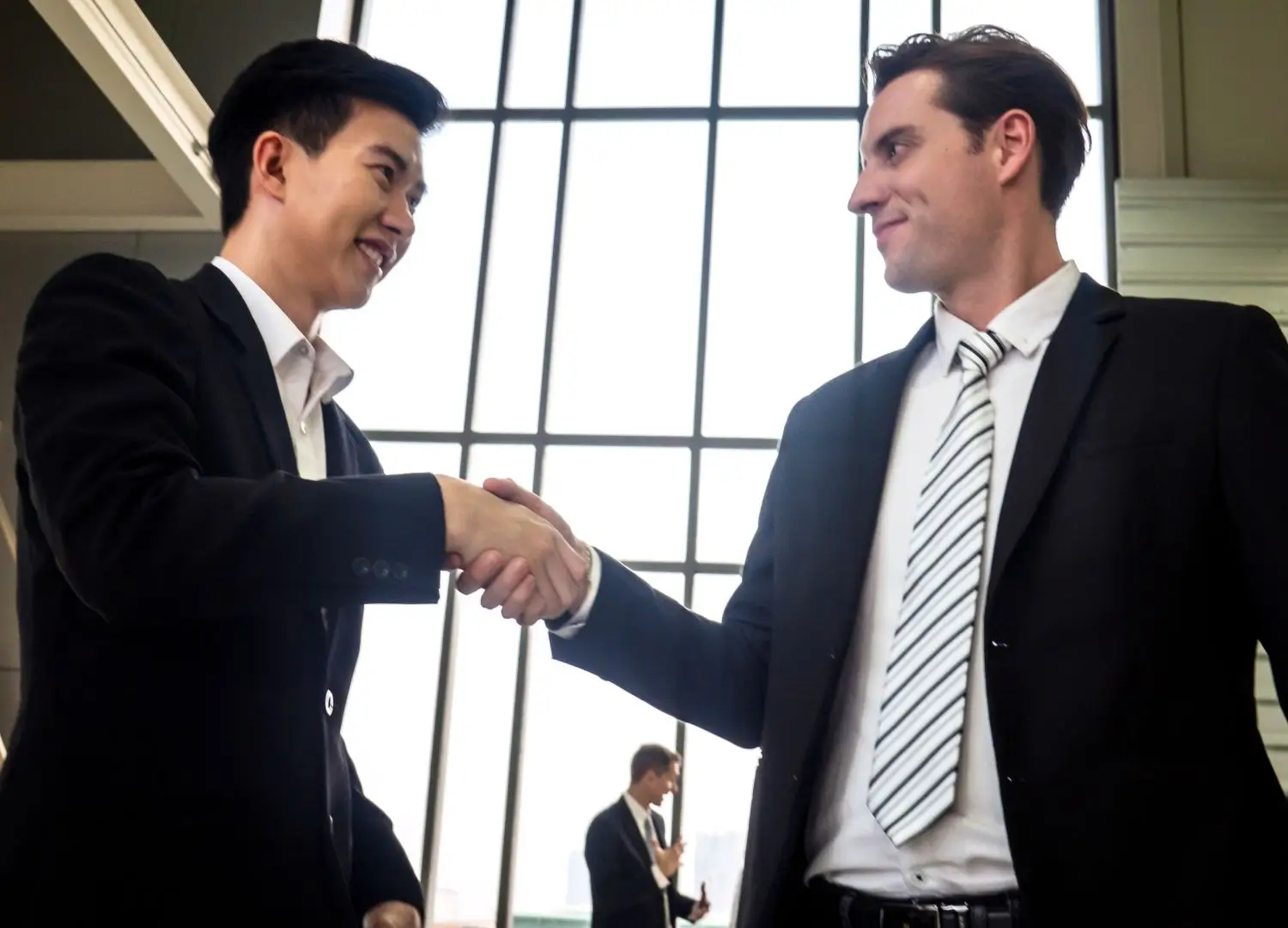 Two business individuals shaking hands in front of a large window