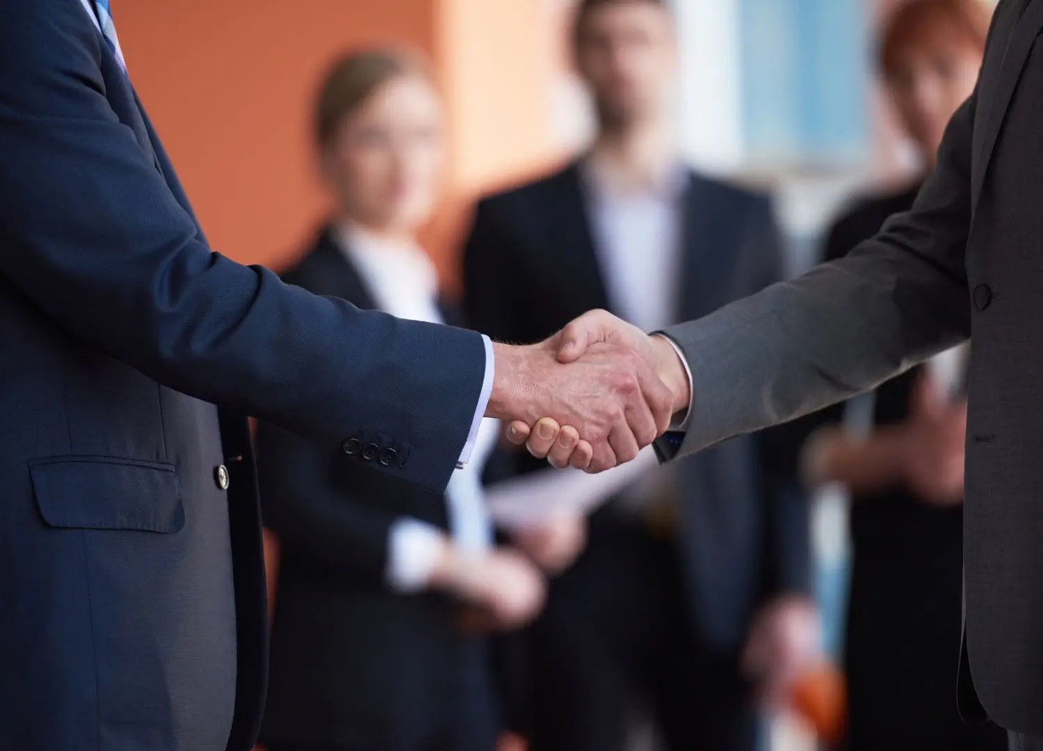 Two business people shaking hands in front of a group of people